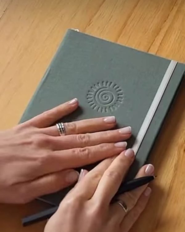 Manos sobre un cuaderno verde con una espiral grabada en la tapa