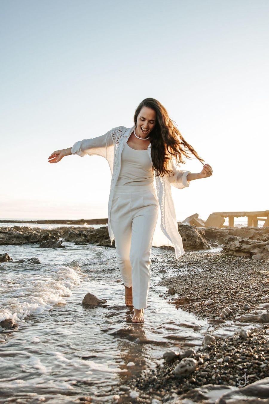 Paula Florez caminando descalza por la orilla del mar, sonriendo, con el pelo al viento