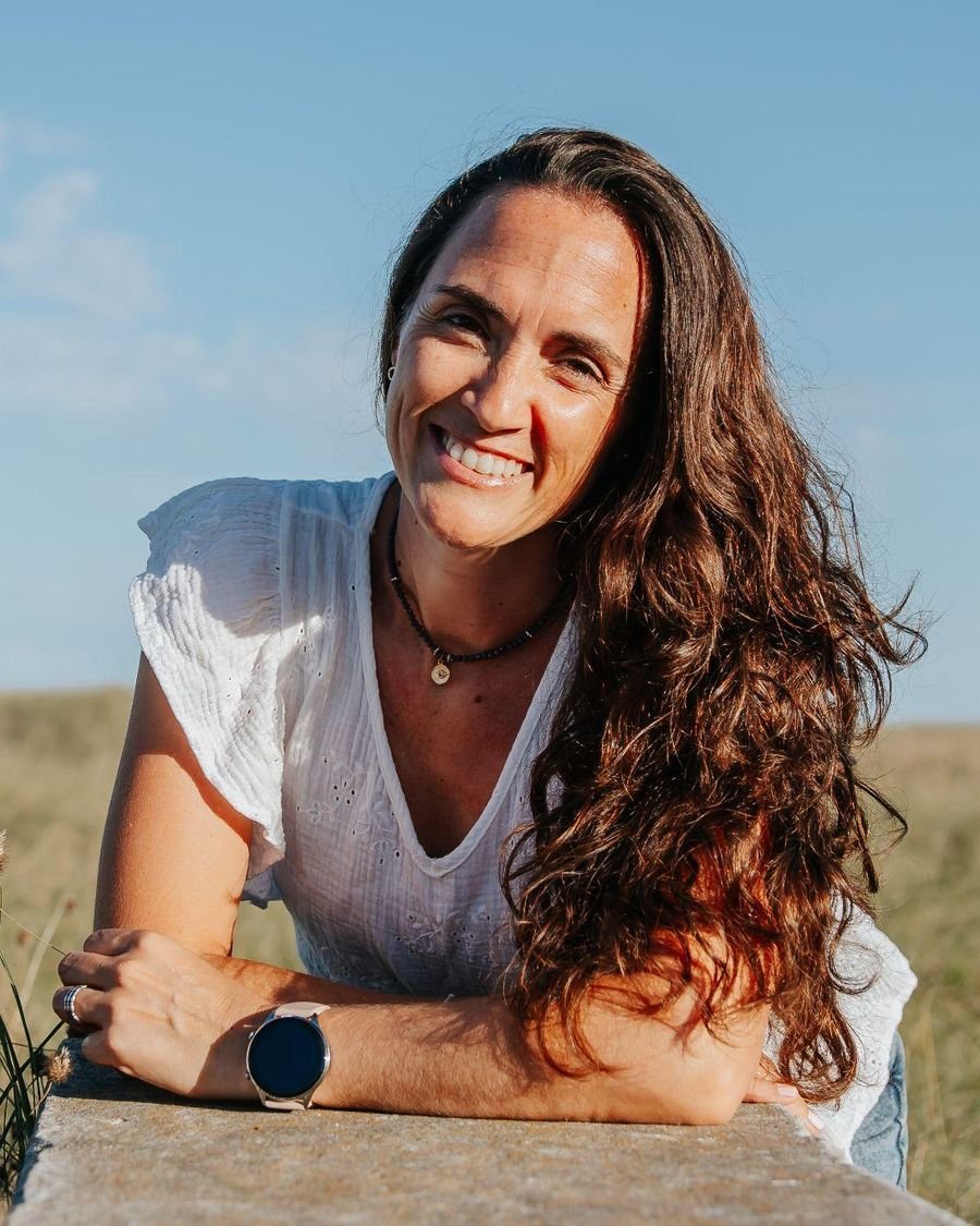 Paula Florez sonriendo, apoyada sobre un muro en el campo, con el cielo de fondo